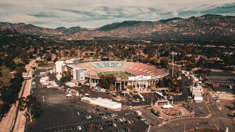 Vista aérea del estadio Rose Bowl, hogar de UCLA, rodeado de montañas y parques, con un estacionamiento visible y un paisaje natural en el fondo. Ideal para eventos deportivos y actividades al aire libre.
