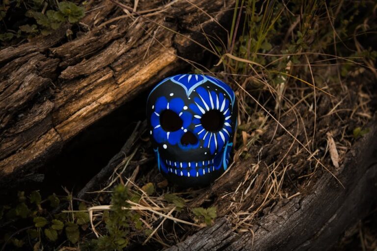 Una calavera de azúcar decorada en colores azul y negro, rodeada de naturaleza y madera en el fondo, que representa la cultura del Día de Muertos.